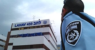 An Israel National Police officer stands outside Lahav 433, the investigative arm of the department, in Lod.  Photo by Federal Bureau of Investigation (FBI) - Israel National Police Officer, Public Domain, https://commons.wikimedia.org/w/index.php?curid=58211714