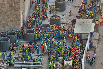 Foreign workers crowding the exit of the Qatar Petroleum District Project in West Bay, Doha.  Photo by Alex Sergeev (www.asergeev.com) - https://www.asergeev.com/pictures/archives/compress/2015/1540/02.htm, CC BY-SA 3.0, https://commons.wikimedia.org/w/index.php?curid=148485758