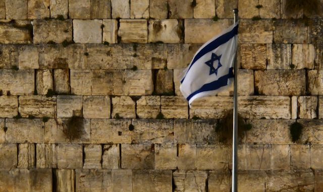Israeli Flag. Photo by <a href="https://unsplash.com/@benjamin_istanbuli?utm_source=unsplash&utm_medium=referral&utm_content=creditCopyText">Benjamin Istanbuli</a> on <a href="https://unsplash.com/photos/a-flag-is-flying-in-front-of-a-wall-of-bricks-ka0NaOfjY0c?utm_source=unsplash&utm_medium=referral&utm_content=creditCopyText">Unsplash</a> 