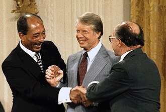 Egyptian President Anwar Sadat (left), U.S. President Jimmy Carter (center), and Israeli Prime Minister Menachem Begin shakes hands at the conclusion of the Camp David Peace Accords signing ceremony in the East Room of the White House on September 17, 1978.  By Not know or unknown - U.S. National Archives and Records Administration, Public Domain, https://commons.wikimedia.org/w/index.php?curid=130042191