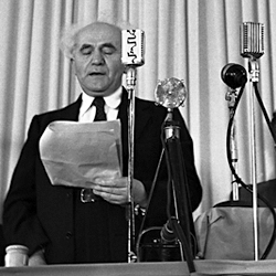 David Ben-Gurion reads the Declaration of Independence at the State Declaration ceremony on May 14, 1948 in front of the microphones of the recording company "Zion" - the two largest microphones identical.  Photo by Rudi Weissenstein -  Public Domain, https://commons.wikimedia.org/w/index.php?curid=22860410